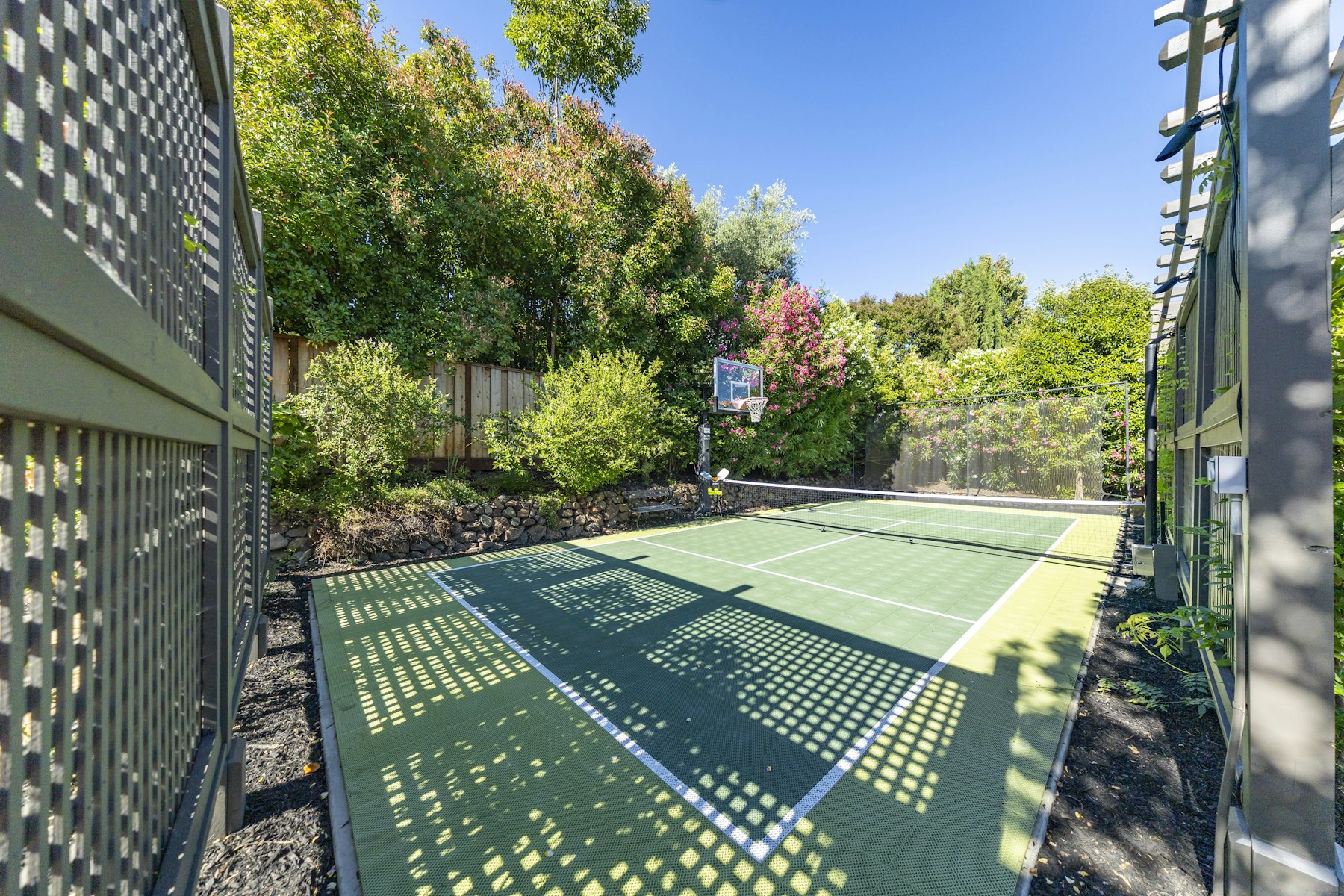Backyard multi-sport court with basketball hoop, pickleball lines, and perimeter fencing